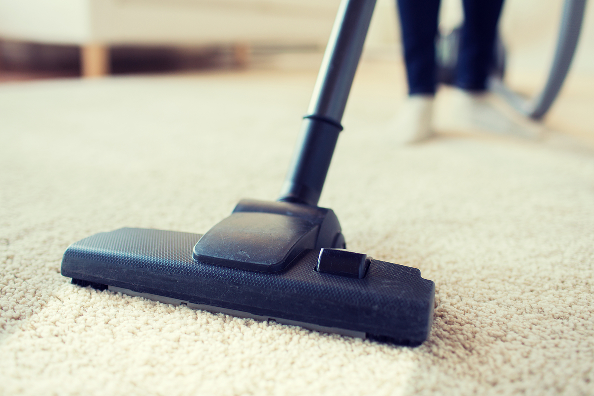 people, housework and housekeeping concept - close up of woman with legs vacuum cleaner cleaning carpet at home