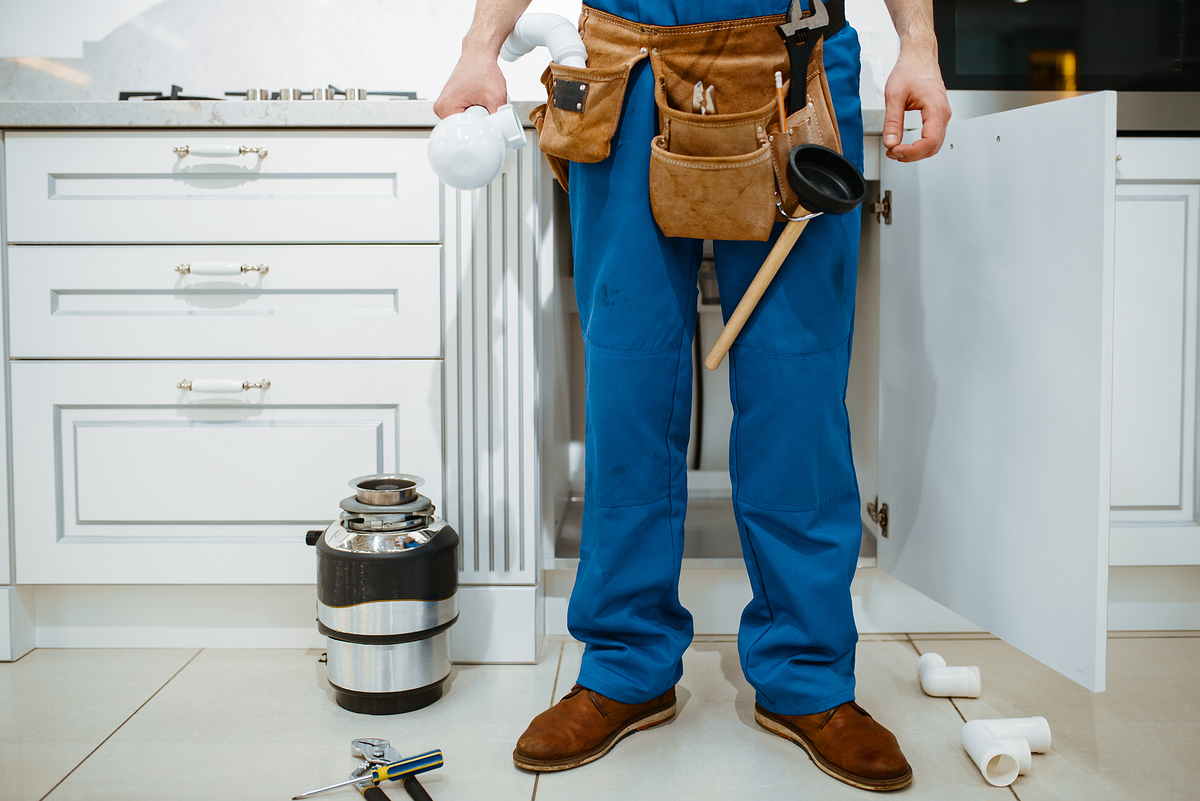 Male plumber installing water filter in the kitchen. Handywoman with toolbag repair sink, sanitary equipment service at home