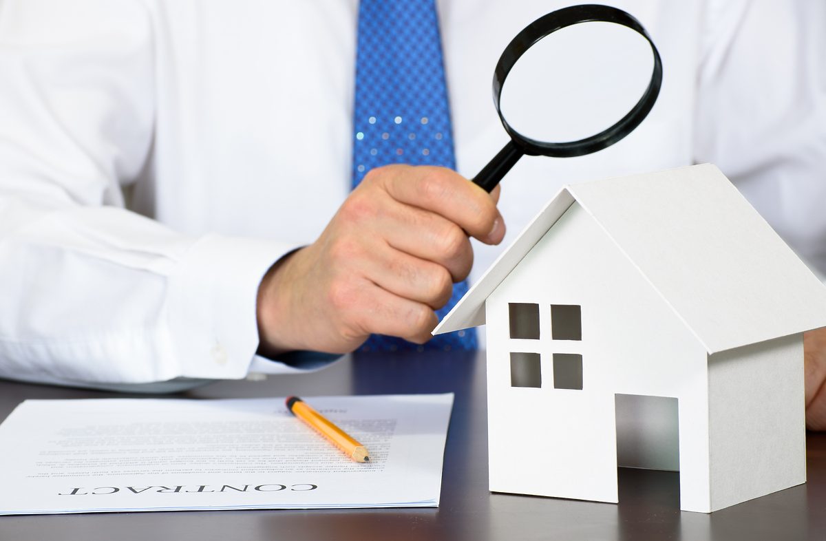 A business man looking at a model house holding a magnifying glass in his hand