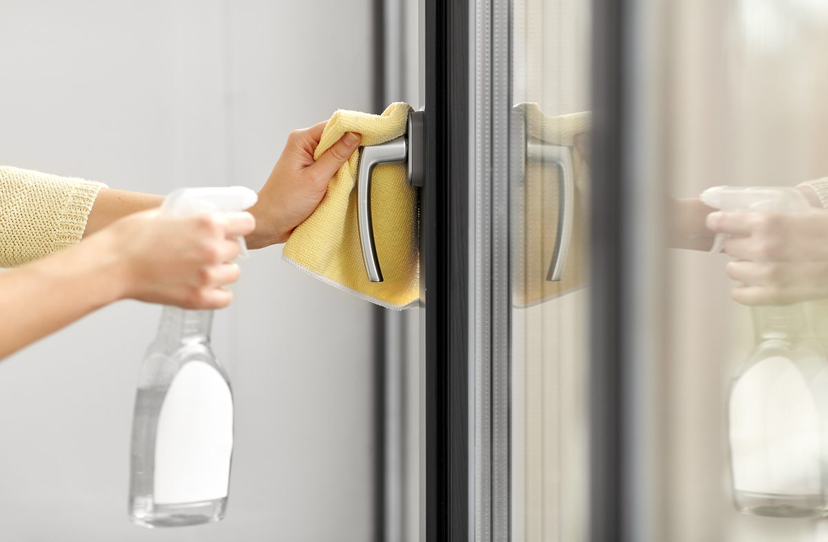 hygiene, health care and safety concept - close up of female hands cleaning window handle surface with disinfectant spray and tissue