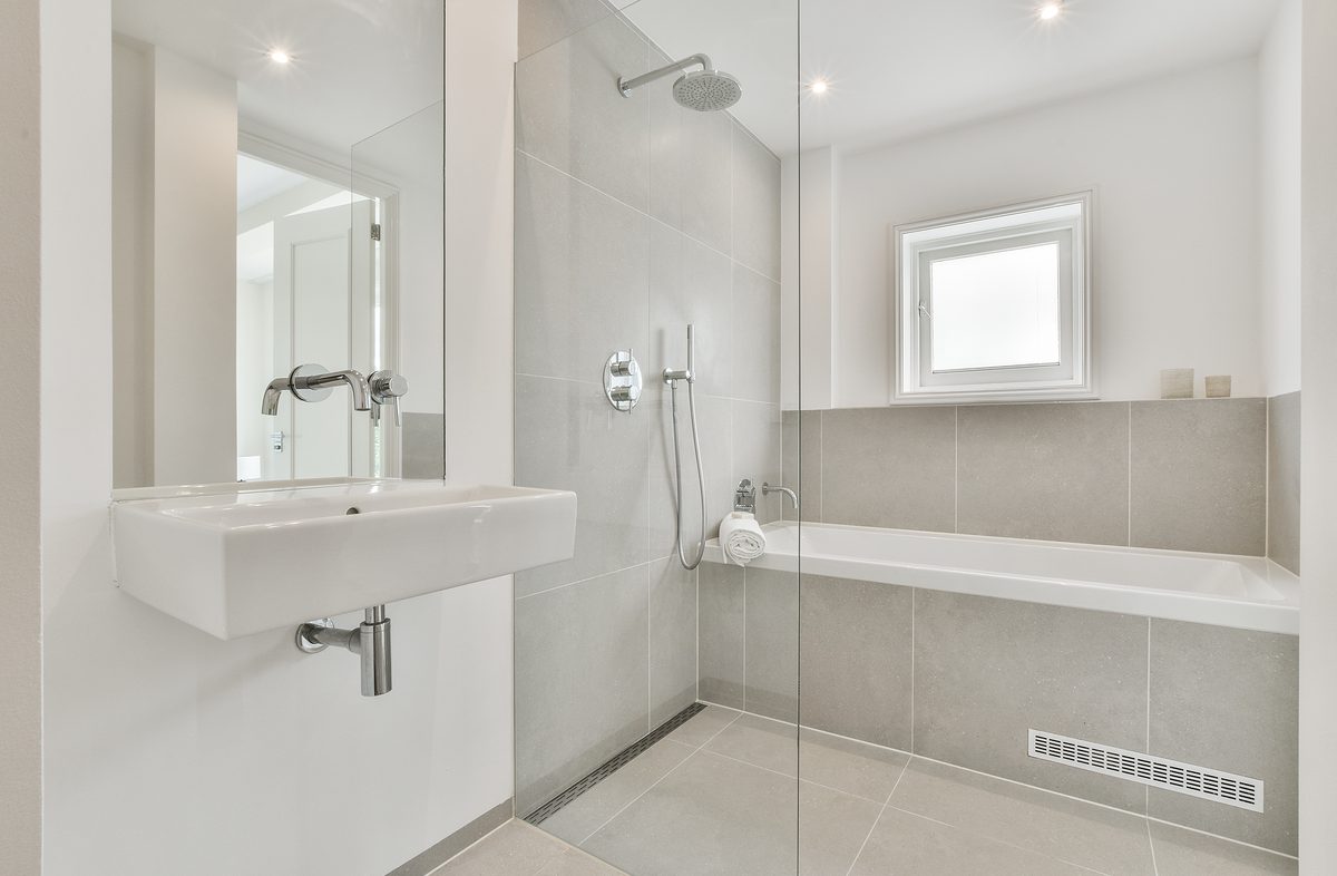 White sink and mirror installed on wall near shower booth with bathtub in modern restroom