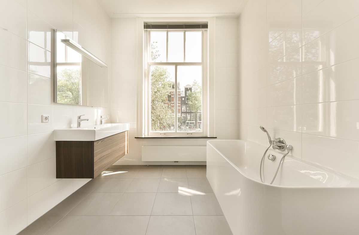 Interior of modern bathroom with mirror and sink with tap and wooden cabinet bathtub and toilet bowl and heated towel rails