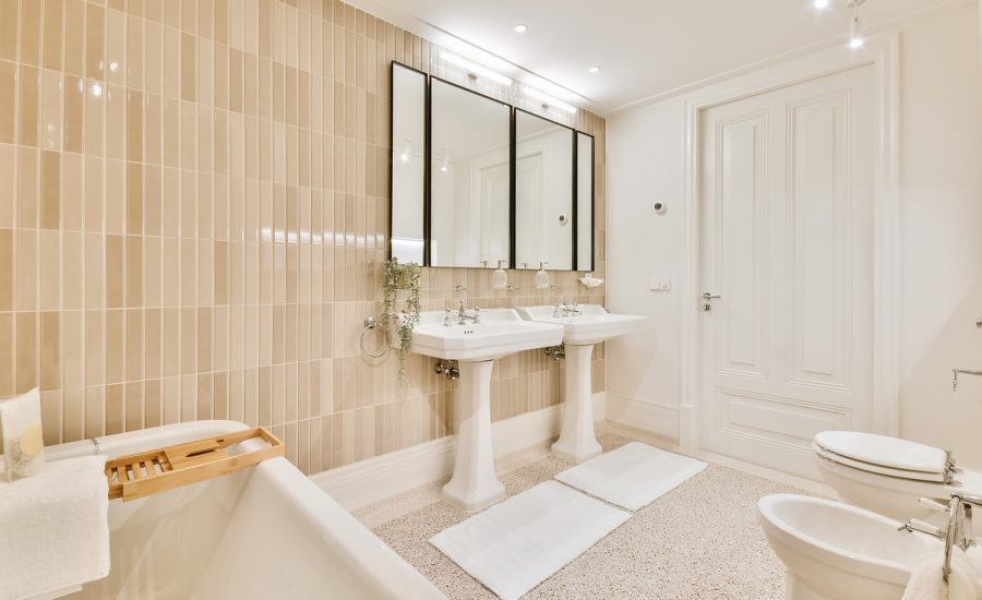 Towel hanging on wooden board placed on ceramic bathtub in contemporary bathroom with mirrors over white sinks and toilet bowl with bidet