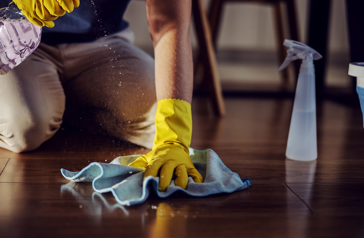 Close up of worthy man kneeling, spraying detergent and cleaning parquet at home.