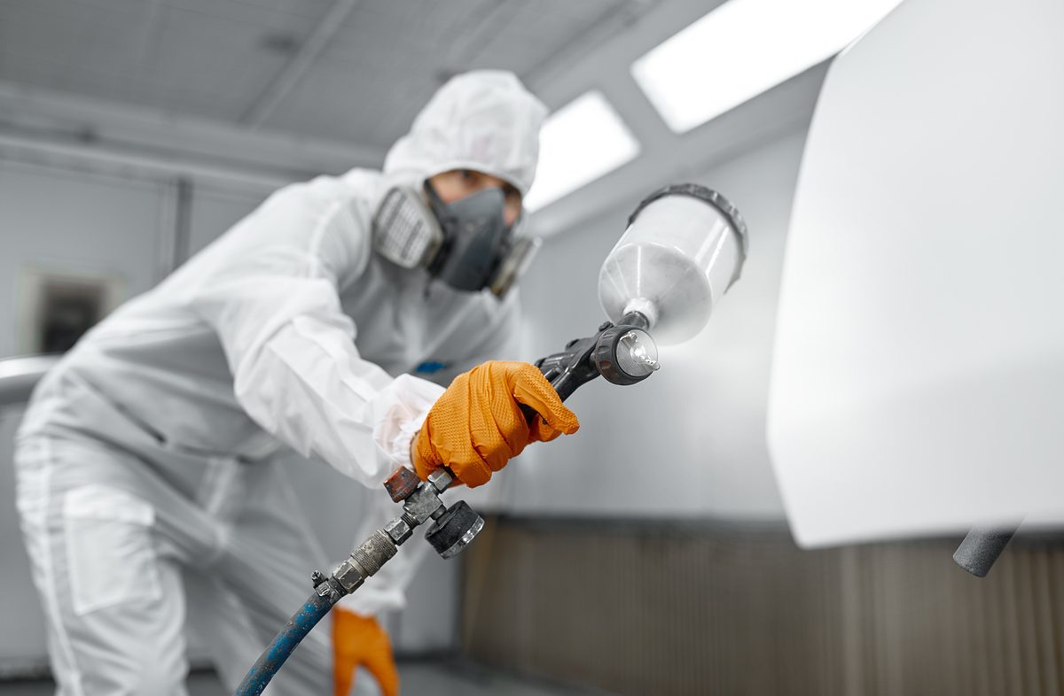 Car painter wearing protective clothes, mask painting automobile door using sprayer. Selective focus