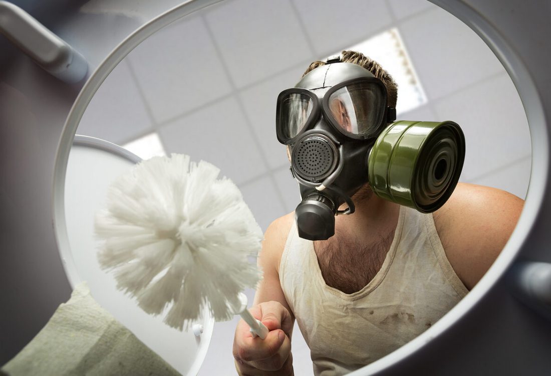 Man in gas mask with brush cleaning the toilet bowl