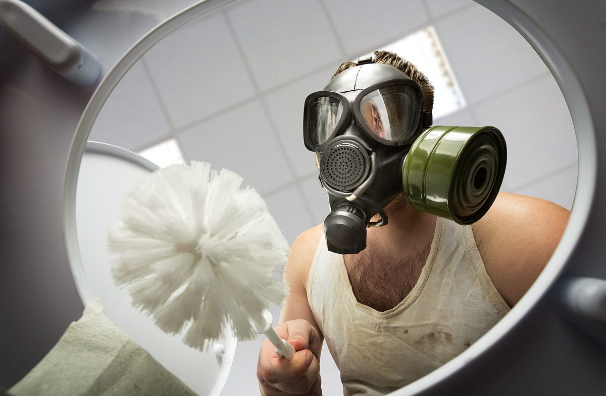 Man in gas mask with brush cleaning the toilet bowl