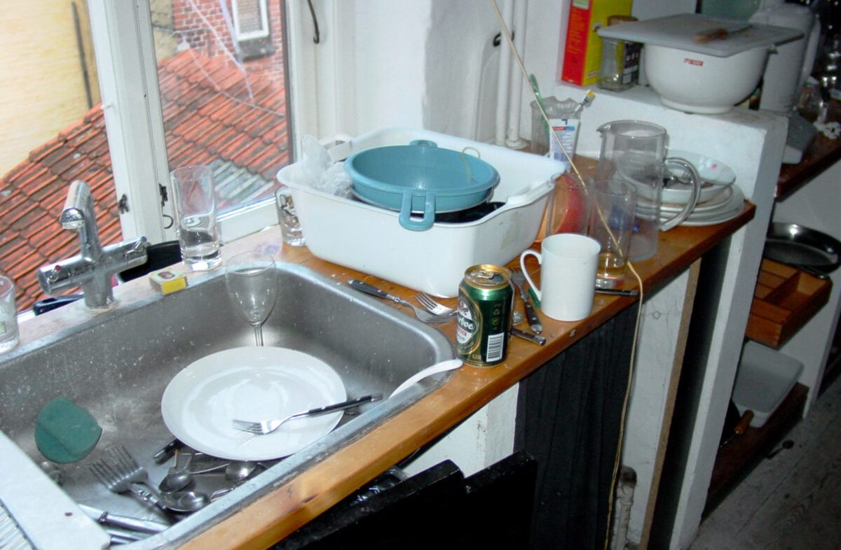 Above messy and untidy kitchen sink with dirty dishes and empty beer bottles after a party. Start cleaning, glasses and cutlery in and around a sink in a filthy kitchen the morning after a fun night.