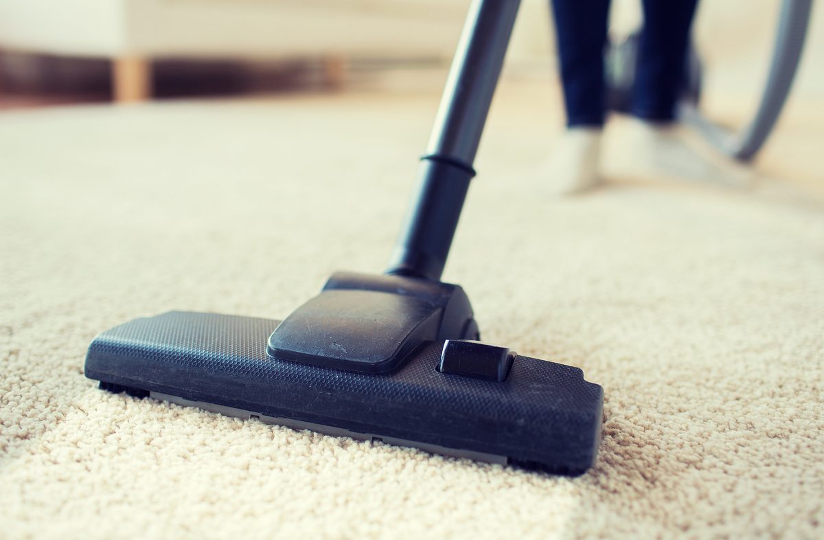 people, housework and housekeeping concept - close up of woman with legs vacuum cleaner cleaning carpet at home