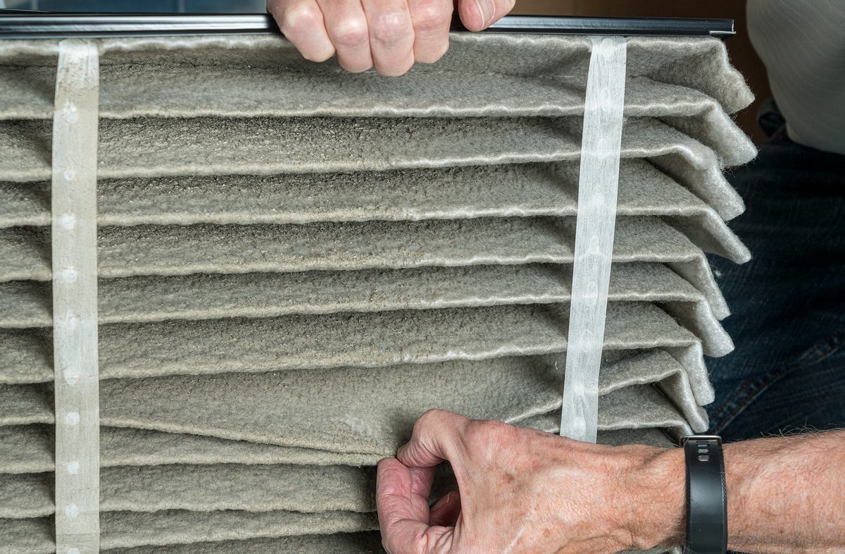 Senior caucasian man looking at the dust in folded dirty air filter in the HVAC furnace system in basement of home