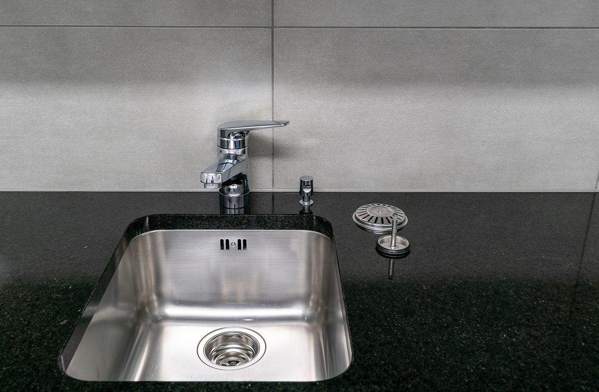 A close up of a very clean kitchen sink and faucet and black quartz stone worktop with strainer and sink stopper