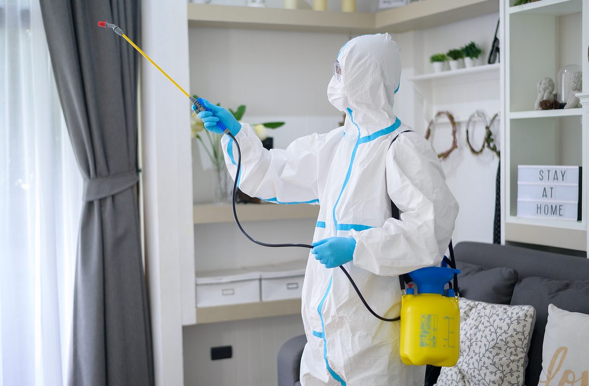 A medical staff in PPE suit is using disinfectant spray in living room, Covid-19 protection , disinfection concept .