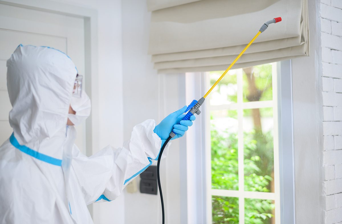 A medical staff in PPE suit is using disinfectant spray in living room, Covid-19 protection , disinfection concept .