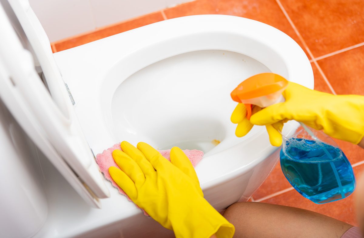 Hand of Asian woman cleaning toilet seat using liquid spray and pink cloth wipe restroom at house, female wearing yellow rubber gloves she sitting cleanup bowl bathroom, Housekeeper healthcare concept