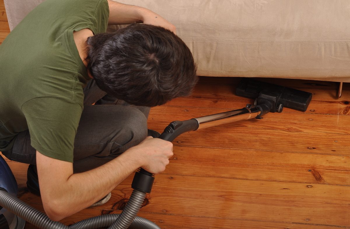 back view of a young man with vacuum cleaner doing the housework